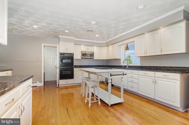 kitchen featuring baseboard heating, stainless steel microwave, crown molding, dobule oven black, and white cabinets