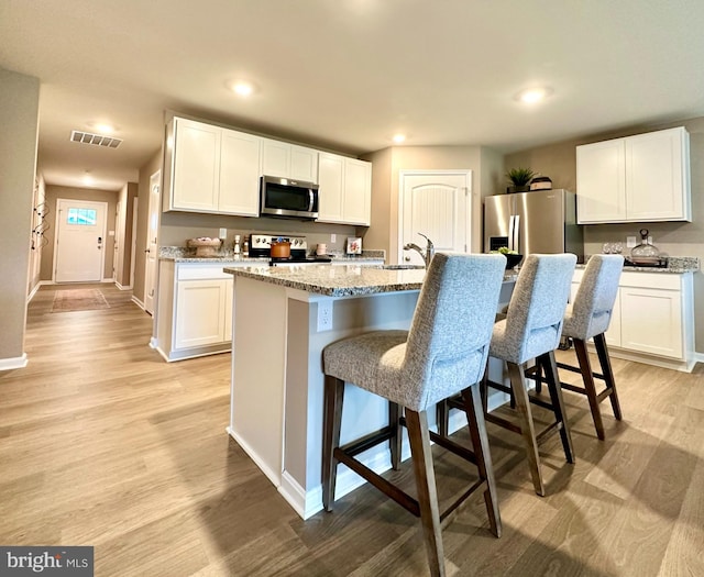 kitchen featuring a breakfast bar area, visible vents, light wood finished floors, stainless steel appliances, and white cabinetry