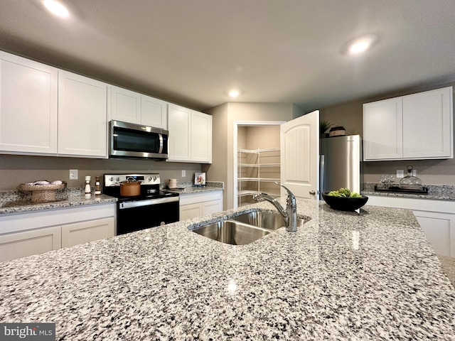 kitchen with range with electric stovetop, a sink, stainless steel microwave, water heater, and white cabinetry