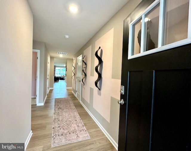 hallway featuring visible vents, baseboards, and wood finished floors