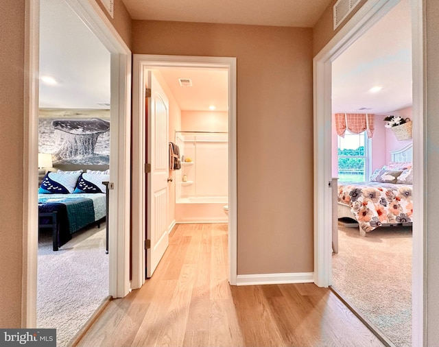 hallway with light wood-style floors, baseboards, and visible vents