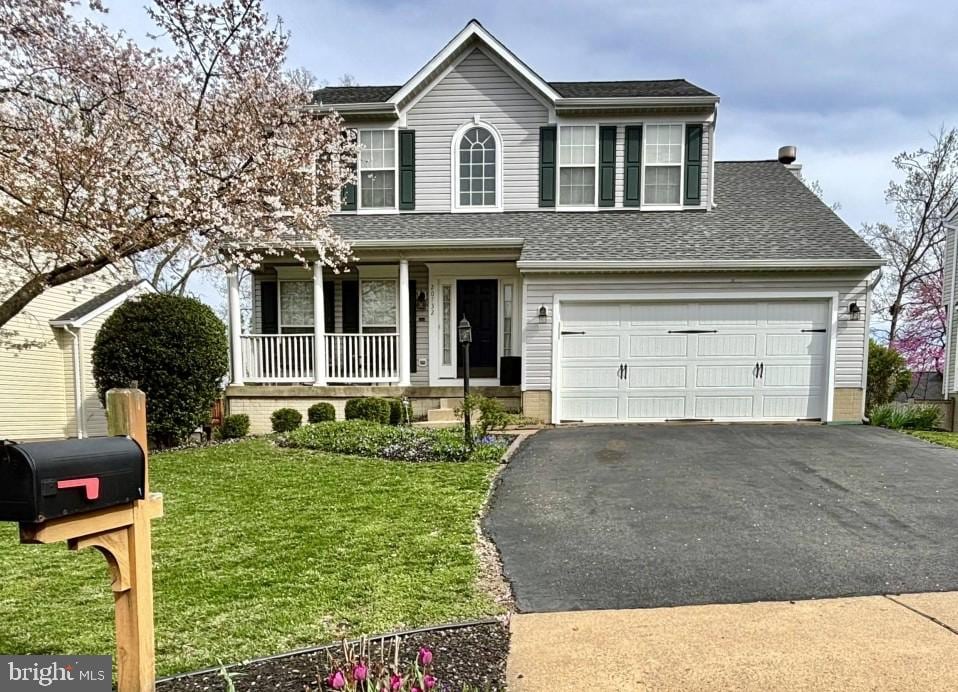 traditional-style house featuring a porch, a shingled roof, a front yard, and aphalt driveway