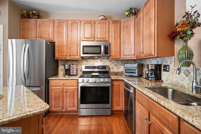 kitchen featuring appliances with stainless steel finishes, light stone counters, a sink, wood finished floors, and a toaster