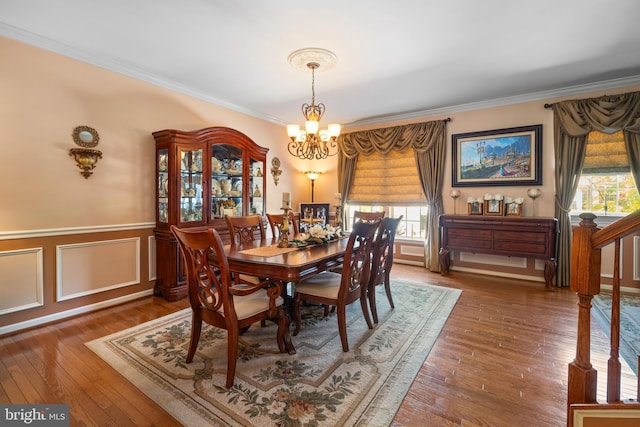 dining space with ornamental molding, wood-type flooring, wainscoting, and a chandelier