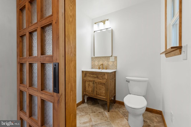 bathroom with backsplash, stone finish flooring, baseboards, vanity, and toilet