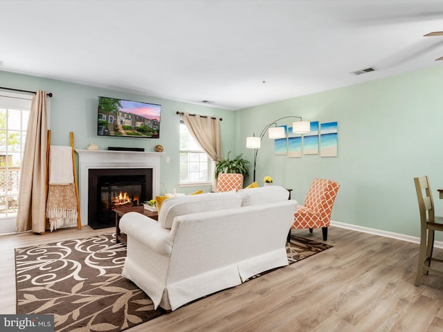 living area featuring a fireplace with flush hearth, baseboards, wood finished floors, and visible vents