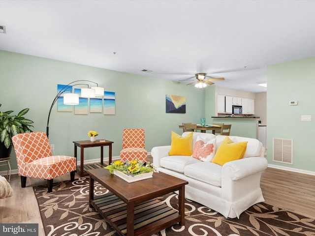 living area featuring a ceiling fan, baseboards, visible vents, and wood finished floors