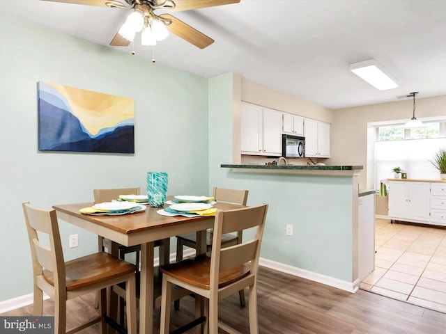 dining space with baseboards, ceiling fan, and light wood-type flooring