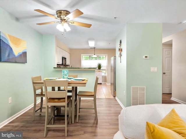 dining area with light wood-style floors, baseboards, ceiling fan, and visible vents