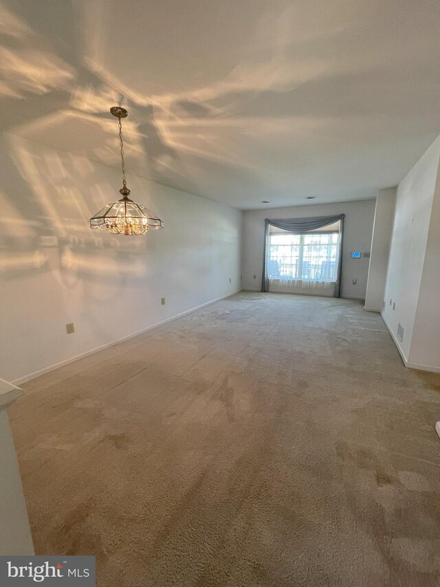 unfurnished room featuring carpet floors, baseboards, and an inviting chandelier