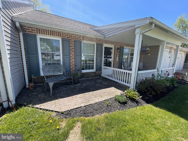 exterior space with a porch, brick siding, a yard, and roof with shingles