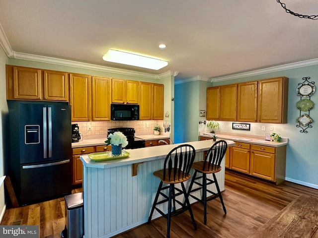 kitchen with black appliances, light countertops, crown molding, and dark wood-type flooring