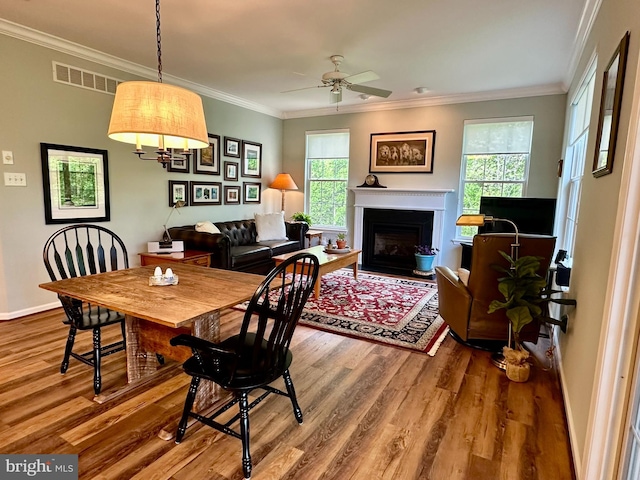 dining room with crown molding, a ceiling fan, a fireplace with flush hearth, and wood finished floors