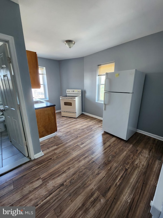 kitchen with baseboards, brown cabinets, dark wood-style floors, and white appliances