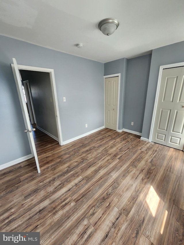unfurnished bedroom featuring baseboards, a closet, and dark wood-style flooring