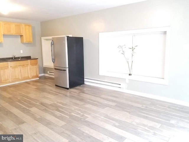 kitchen with dark countertops, a sink, baseboard heating, light brown cabinets, and freestanding refrigerator