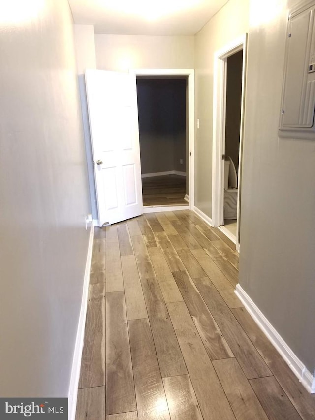 corridor with baseboards, electric panel, and wood finished floors