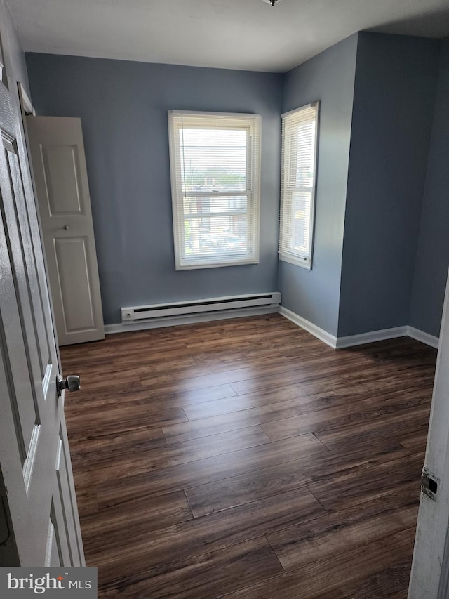 unfurnished room featuring dark wood-type flooring, baseboards, and a baseboard heating unit