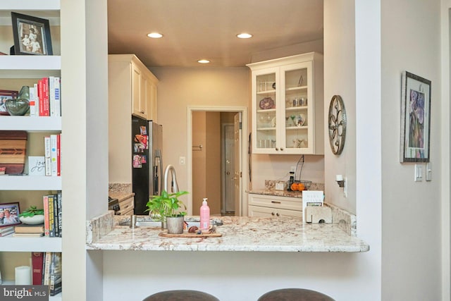 kitchen featuring light stone countertops, recessed lighting, glass insert cabinets, a peninsula, and stainless steel fridge