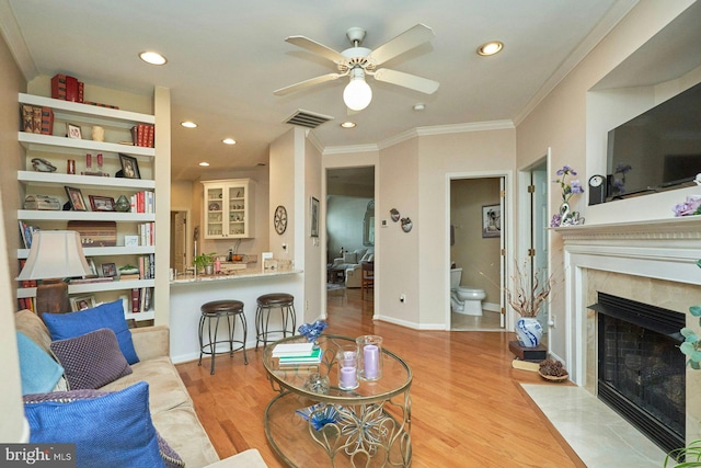 living area with wood finished floors, a fireplace, crown molding, visible vents, and ceiling fan