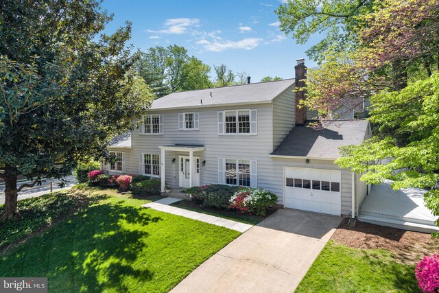 colonial inspired home featuring a chimney, a garage, driveway, and a front yard