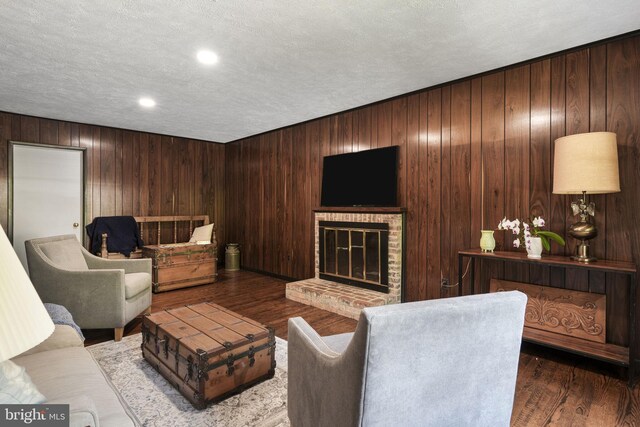 living area with a fireplace, wood walls, a textured ceiling, and wood finished floors