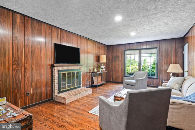 living area featuring wood finished floors, a fireplace, baseboards, wooden walls, and a textured ceiling