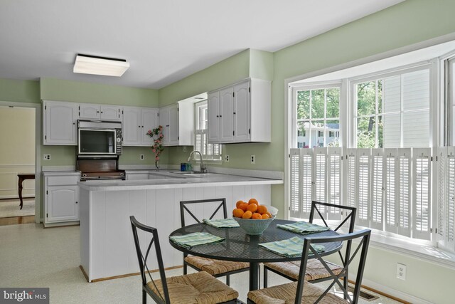 kitchen with a sink, light countertops, range, a peninsula, and white cabinetry