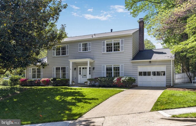 colonial-style house featuring driveway, a chimney, a front lawn, and a garage