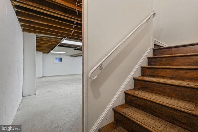 staircase with unfinished concrete floors and concrete block wall