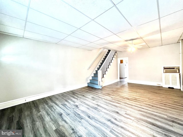 below grade area featuring ceiling fan, a paneled ceiling, baseboards, wood finished floors, and stairway