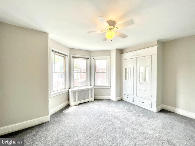 unfurnished bedroom featuring carpet floors, a ceiling fan, baseboards, and radiator heating unit