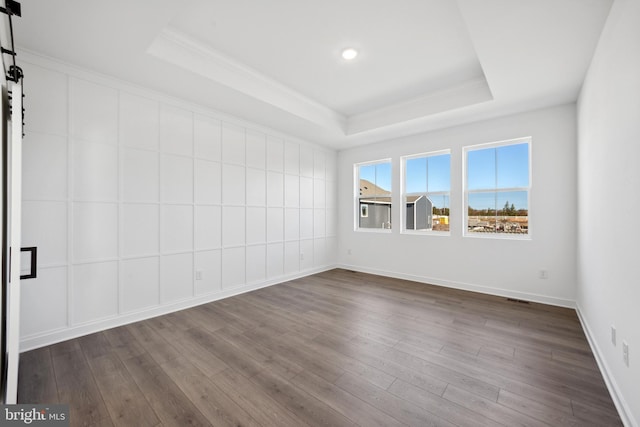 empty room featuring a barn door, ornamental molding, baseboards, a tray ceiling, and dark wood-style floors