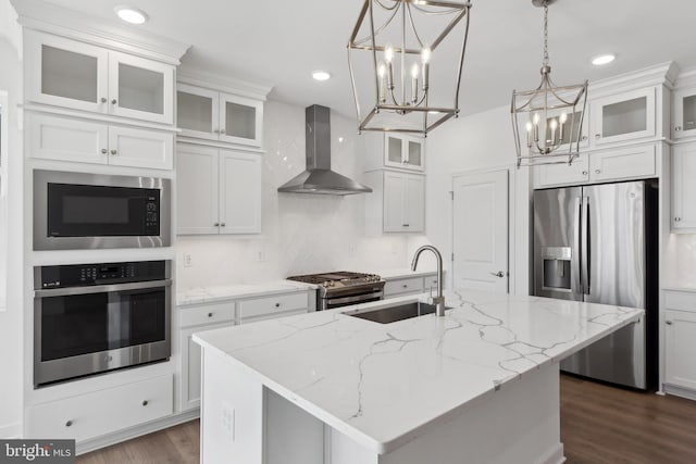 kitchen featuring dark wood-style floors, wall chimney exhaust hood, a sink, a notable chandelier, and stainless steel appliances