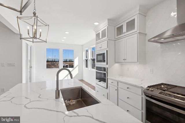 kitchen with wall chimney range hood, a chandelier, tasteful backsplash, a sink, and stainless steel appliances