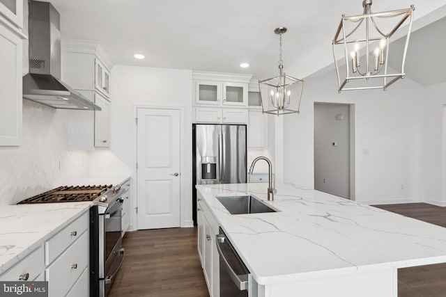 kitchen with an inviting chandelier, a kitchen island with sink, wall chimney exhaust hood, a sink, and appliances with stainless steel finishes