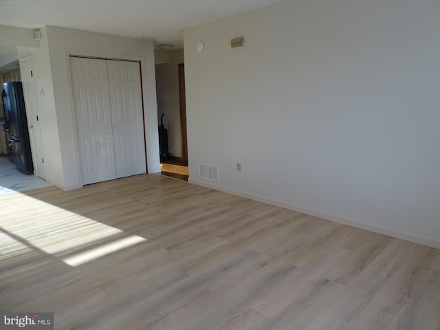 unfurnished bedroom with visible vents, freestanding refrigerator, a closet, and light wood-type flooring