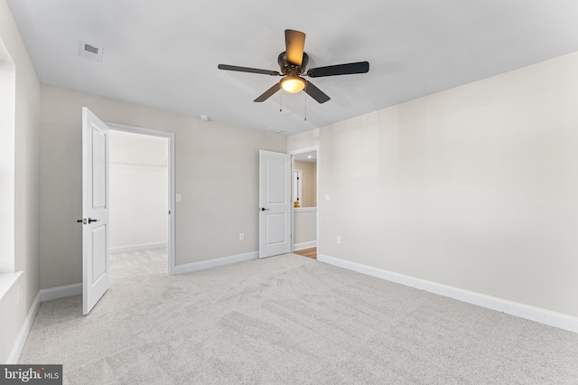 unfurnished bedroom featuring a walk in closet, a ceiling fan, baseboards, a closet, and light carpet