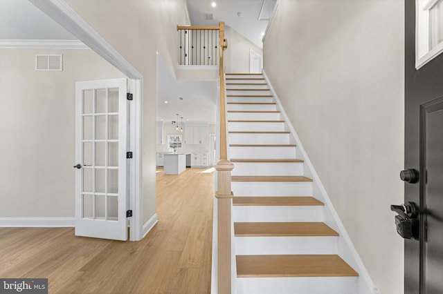 stairway with visible vents, baseboards, a towering ceiling, and wood finished floors