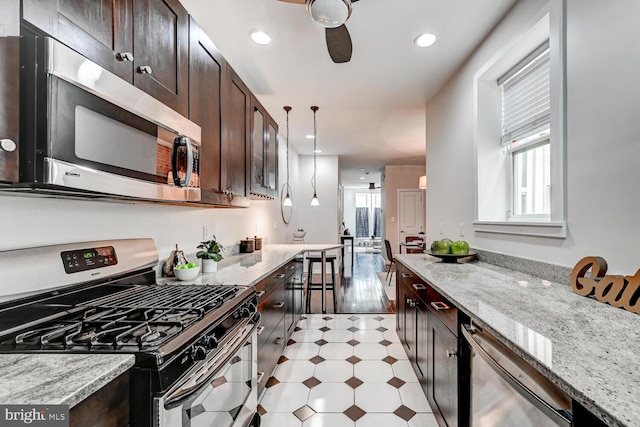 136 W Ostend St, Baltimore, MD 21230 - kitchen featuring appliances with stainless steel finishes, light floors, dark brown cabinets, light stone counters, and hanging light fixtures