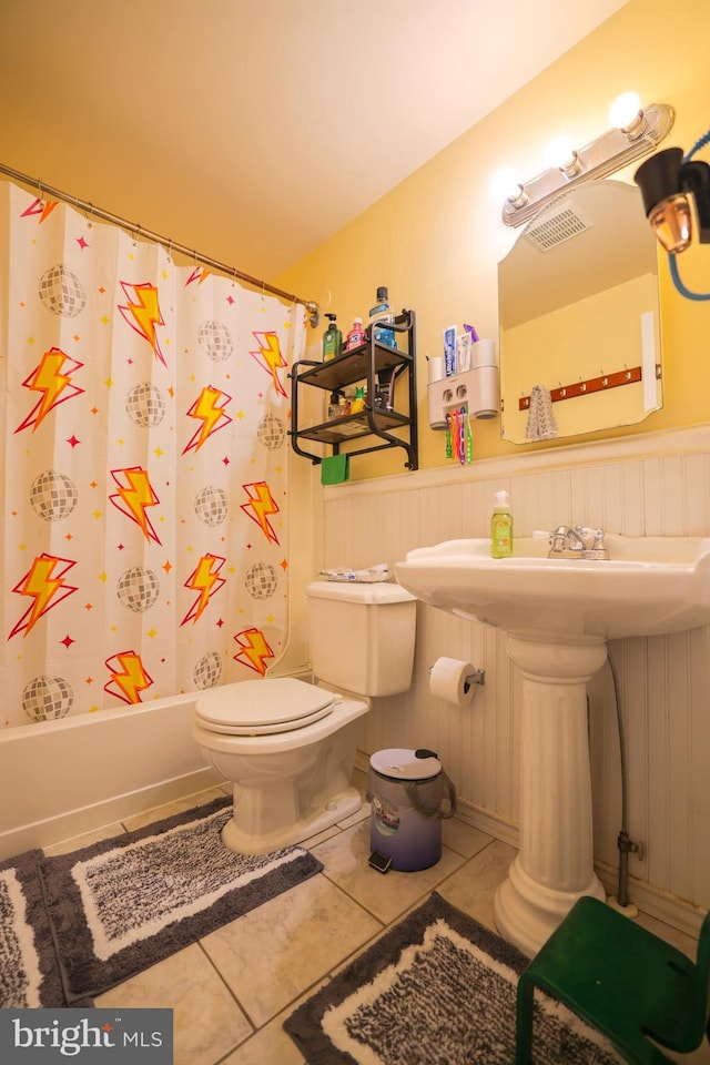 full bathroom with toilet, tile patterned floors, and a wainscoted wall
