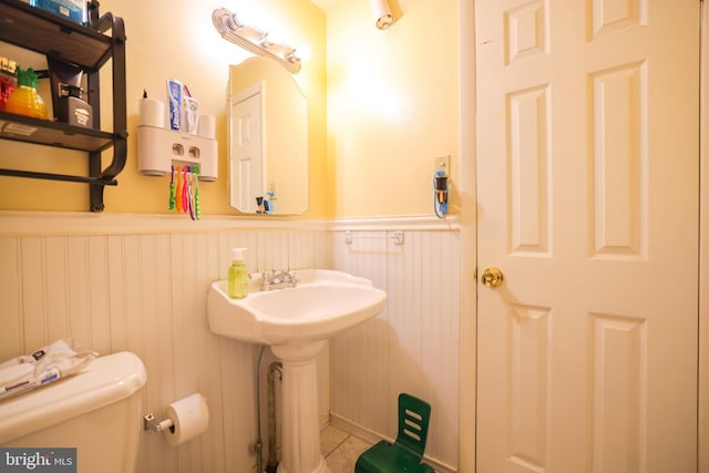 half bath featuring a wainscoted wall, tile patterned flooring, and toilet