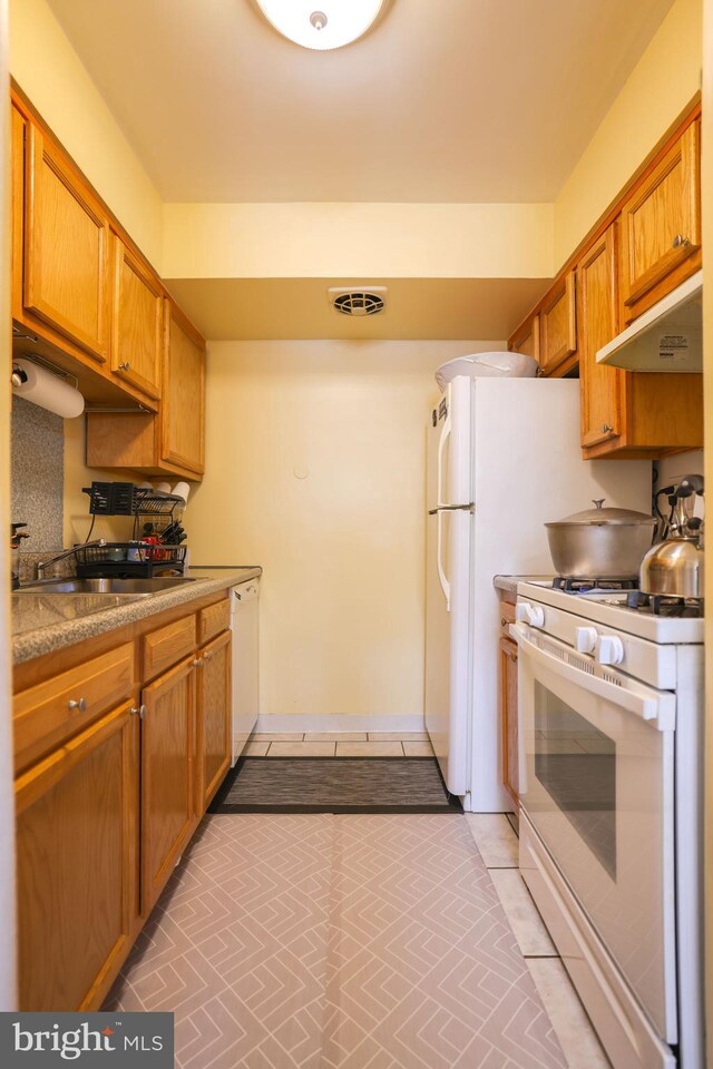 kitchen featuring brown cabinets, white appliances, light countertops, under cabinet range hood, and visible vents