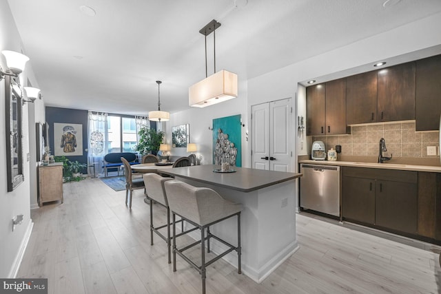 kitchen featuring a breakfast bar area, dark brown cabinetry, tasteful backsplash, stainless steel dishwasher, and a sink