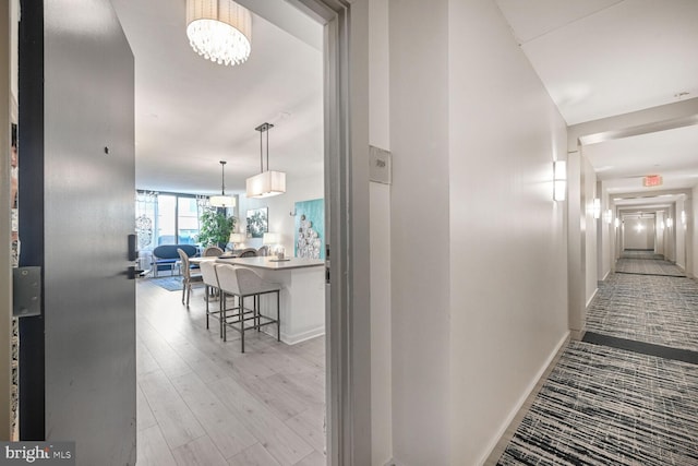 corridor with baseboards, a notable chandelier, and light wood-style floors