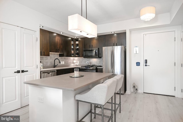 kitchen with decorative backsplash, appliances with stainless steel finishes, dark brown cabinets, and a breakfast bar