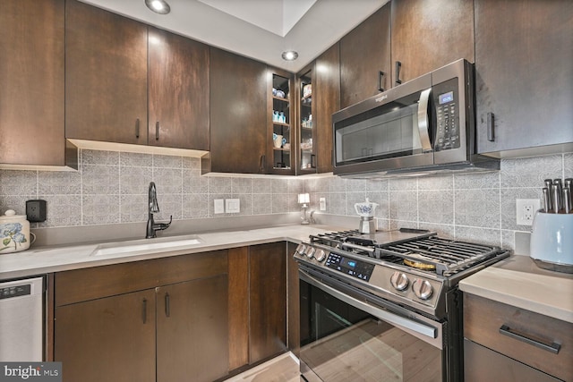 kitchen featuring appliances with stainless steel finishes, tasteful backsplash, dark brown cabinets, a sink, and light countertops