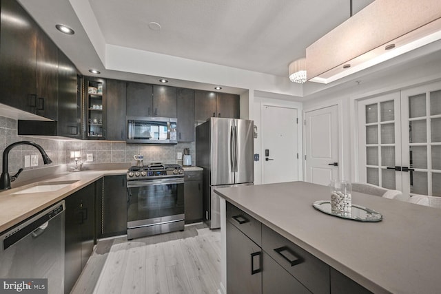 kitchen featuring decorative backsplash, light wood-type flooring, a sink, glass insert cabinets, and stainless steel appliances