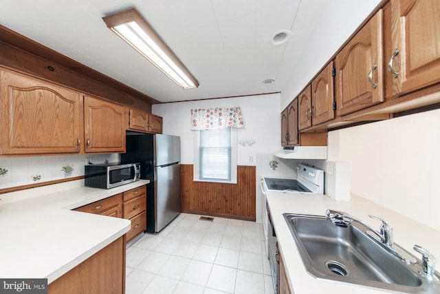 kitchen with a sink, stainless steel appliances, light countertops, and a wainscoted wall