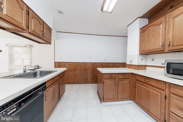 kitchen featuring dishwasher, a sink, a peninsula, a wainscoted wall, and light countertops